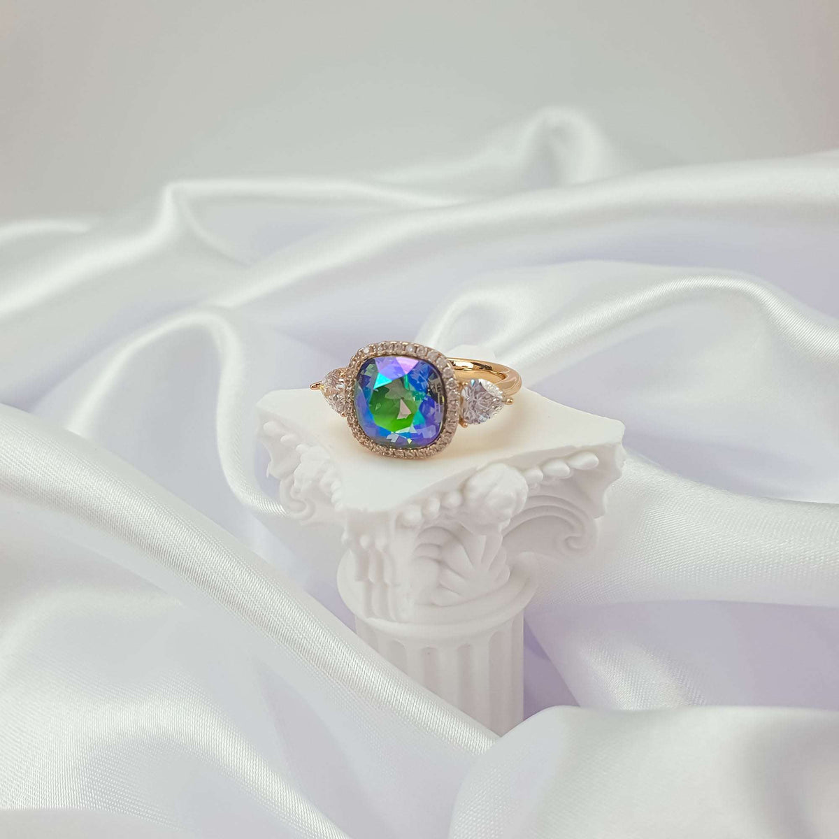 Ring with a blue-green crystal on a white plaster column and satin fabric