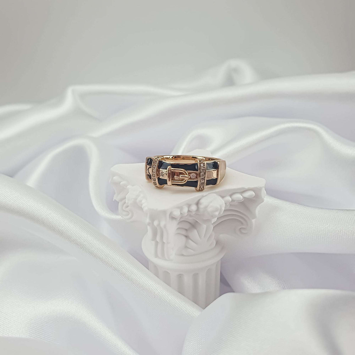 Gold-plated belt buckle ring with black enamel and cubic zirconia on a stand