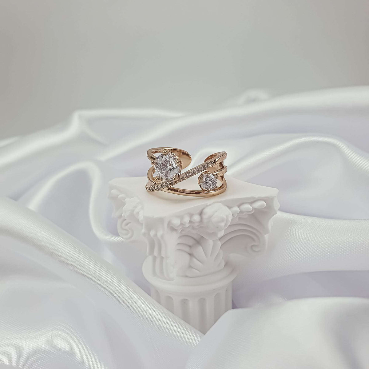 Crossover ring with cubic zirconia, side view on a white stand and silk