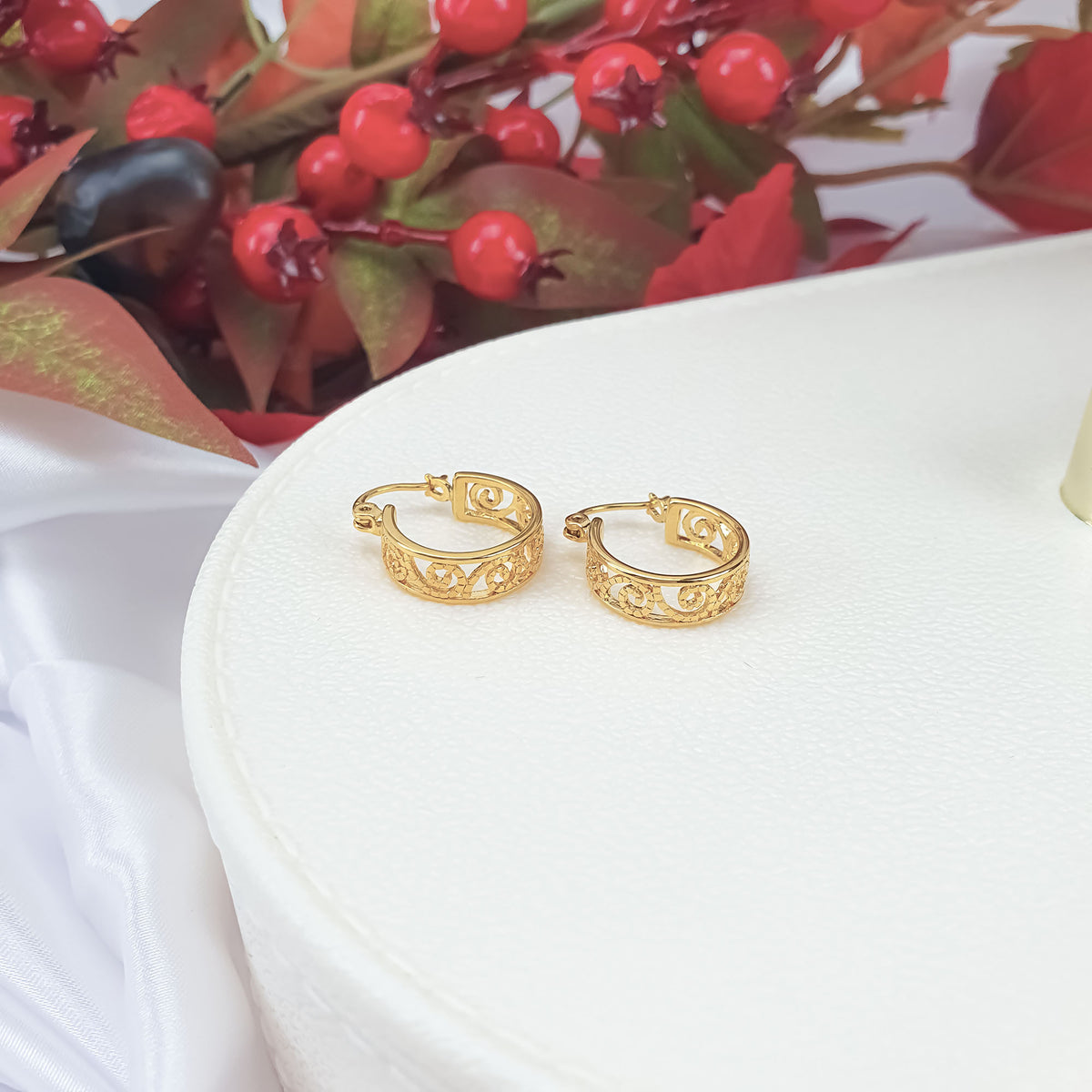 Gold-plated openwork spiral earrings on a white box with red berries