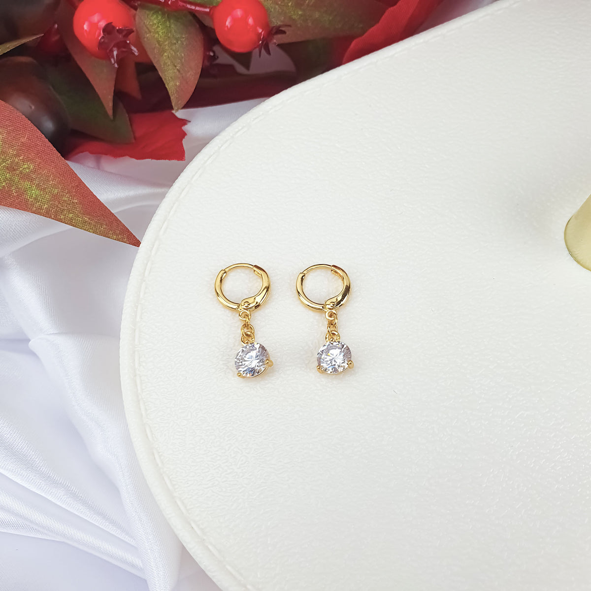 Two gold-plated earrings with hanging white cubic zirconia on a stand