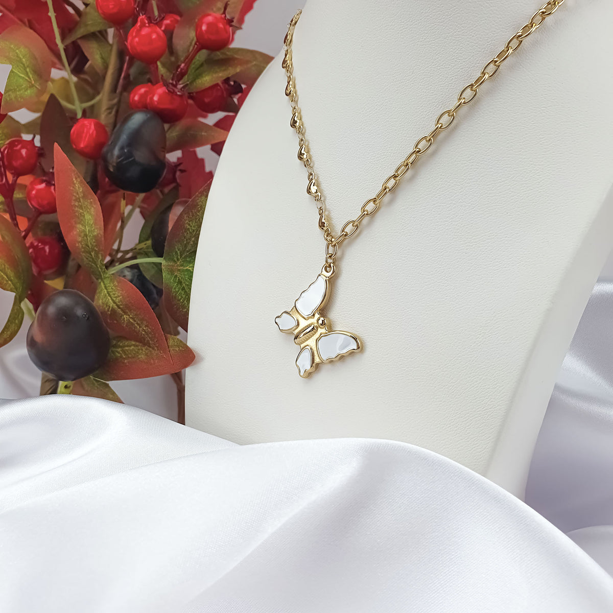 Gold-plated enamel butterfly pendant on a white jewellery bust with berries