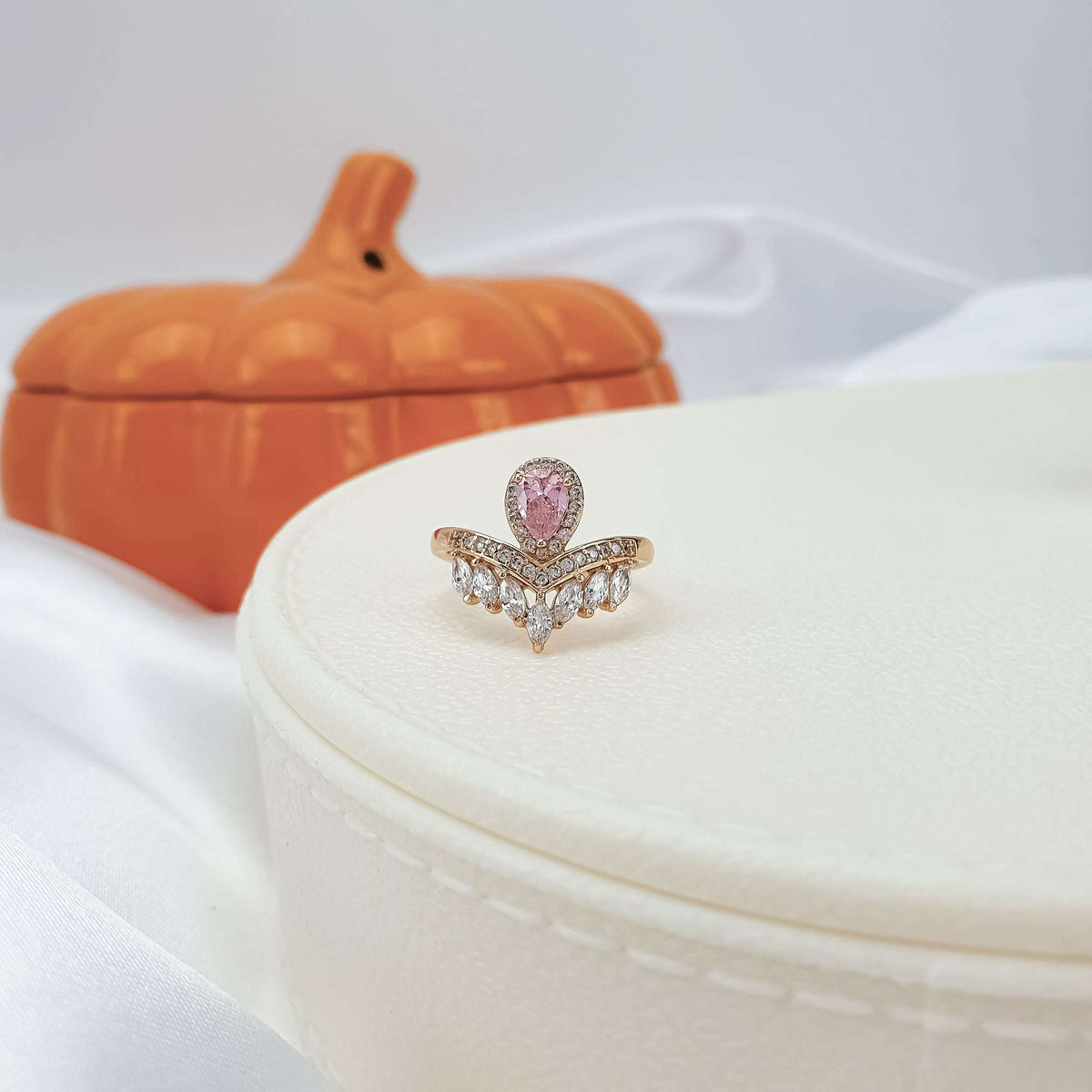 Pink cubic zirconia ring on a light jewellery box, orange pumpkin behind