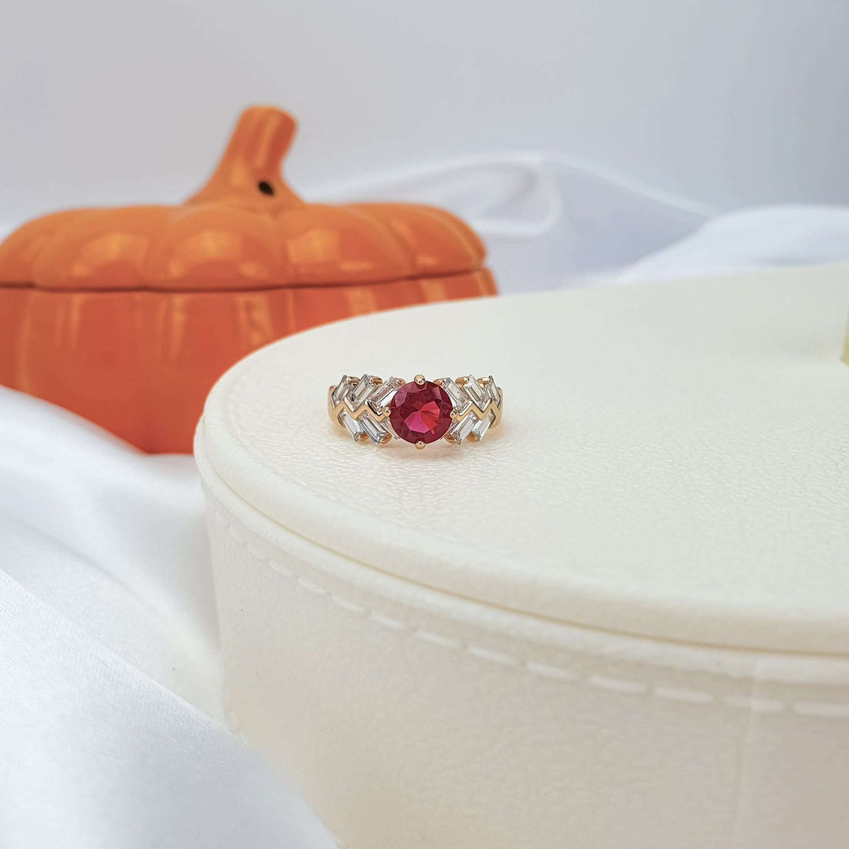 Red stone ring with geometric baguettes on a box in an autumn setting