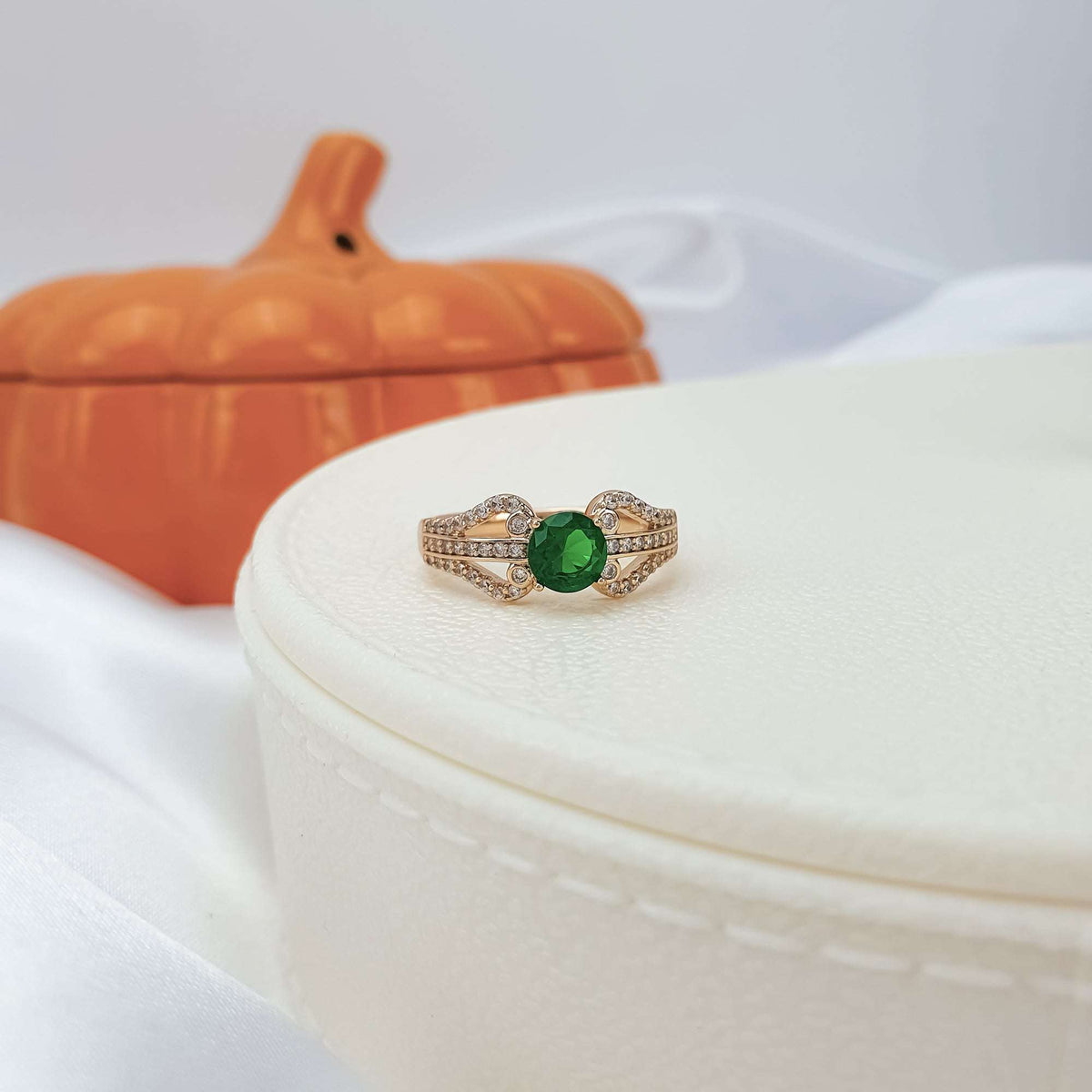 Green cubic zirconia ring on a white jewellery box, orange pumpkin behind