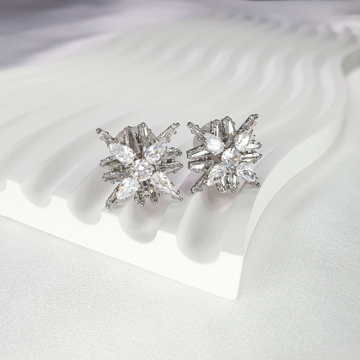 Silver-tone snowflake clip-on earrings with white cubic zirconia on a stand