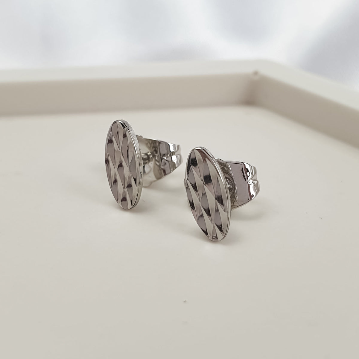 Elongated oval silver-tone studs with a diamond-cut texture on a light tray