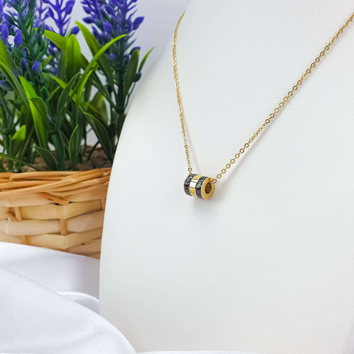 Gold-plated necklace with a black stone cylinder on a white display bust