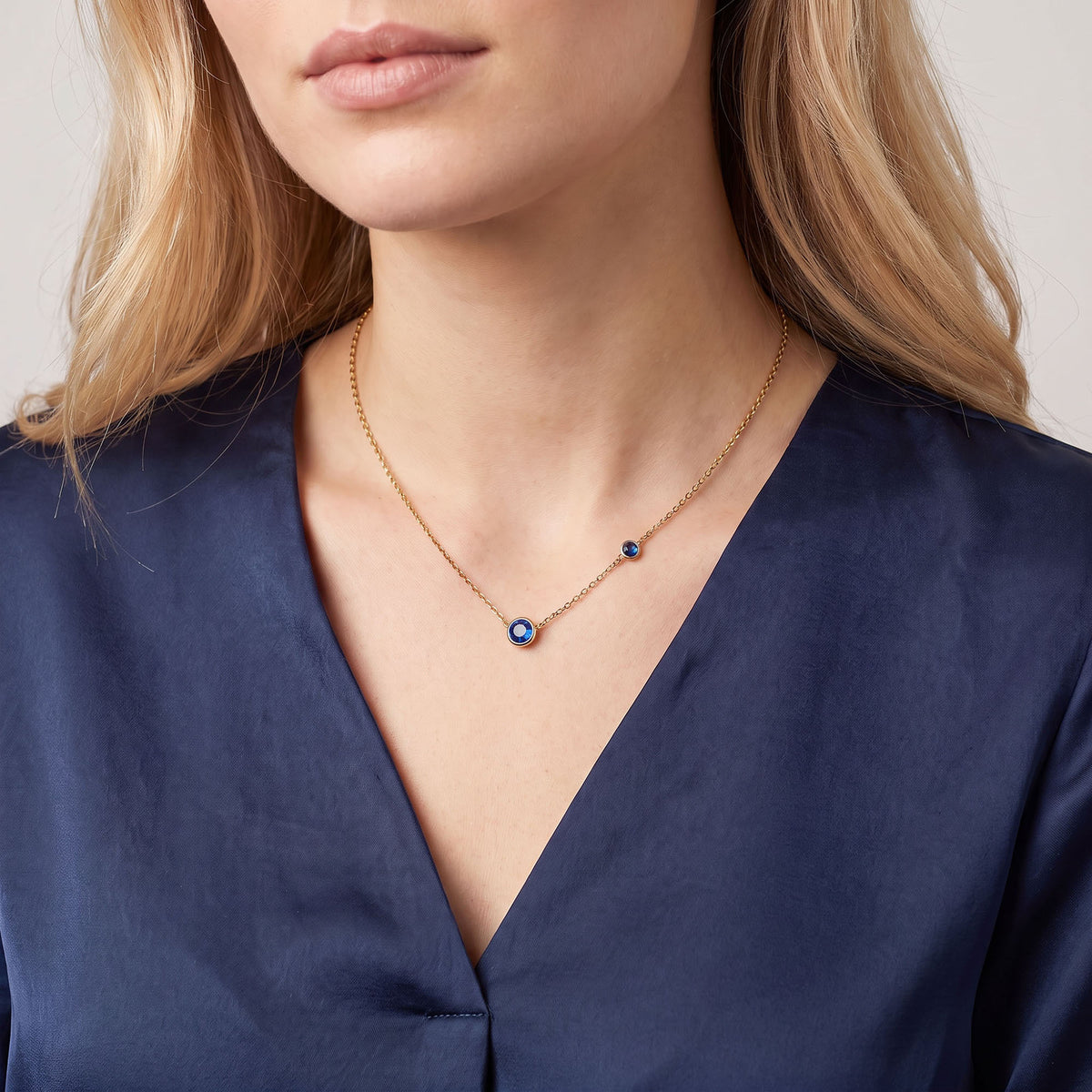Gold-plated necklace with two blue cubic zirconia on a model wearing a navy blouse