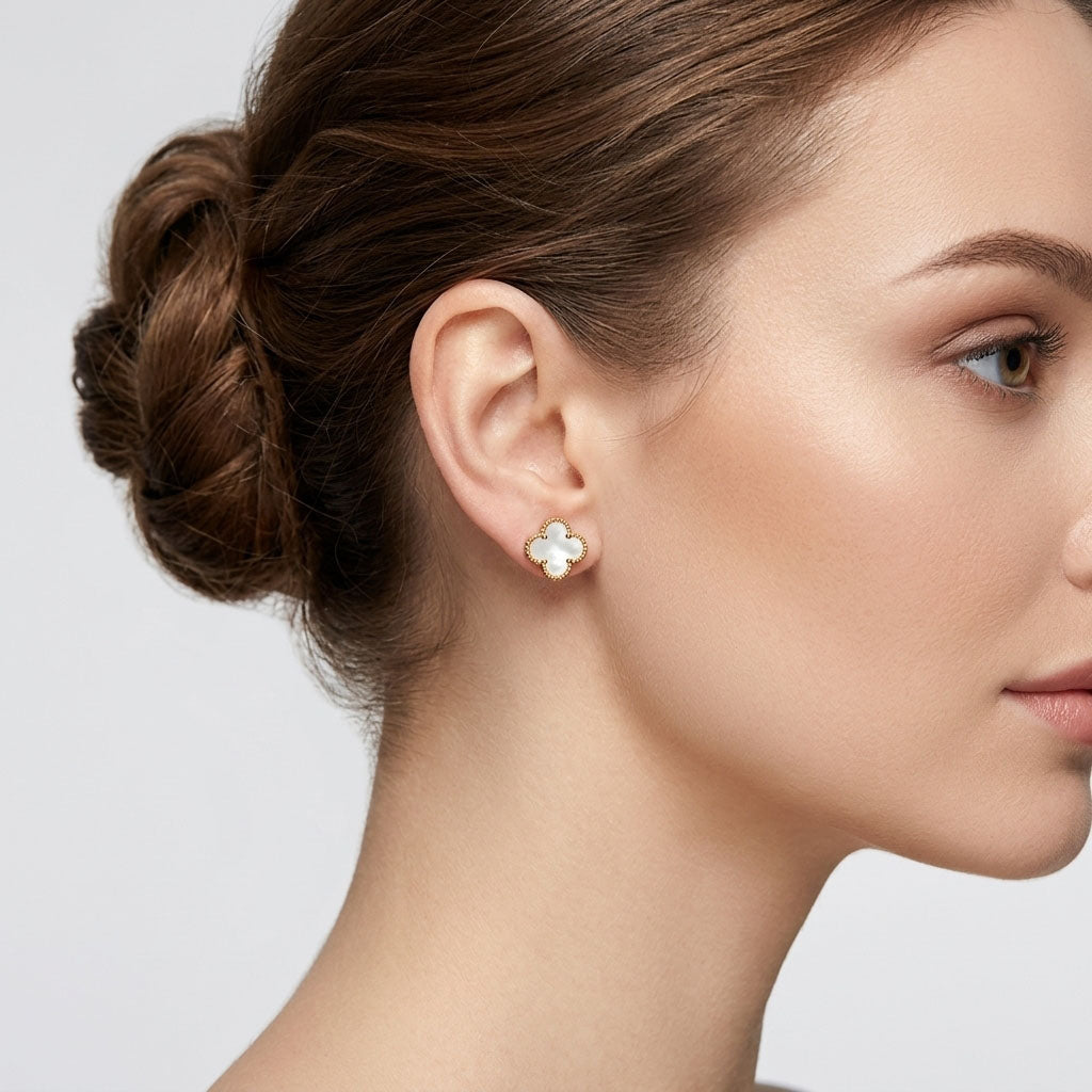 White enamel four-leaf clover earring on an earlobe with a gold-tone border