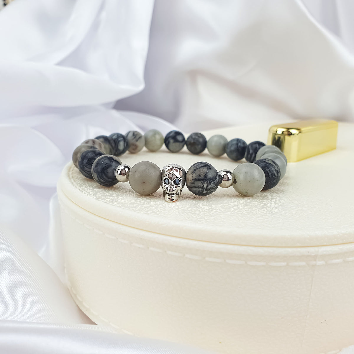 Grey stone bead bracelet with a silver-tone skull on a light jewellery box