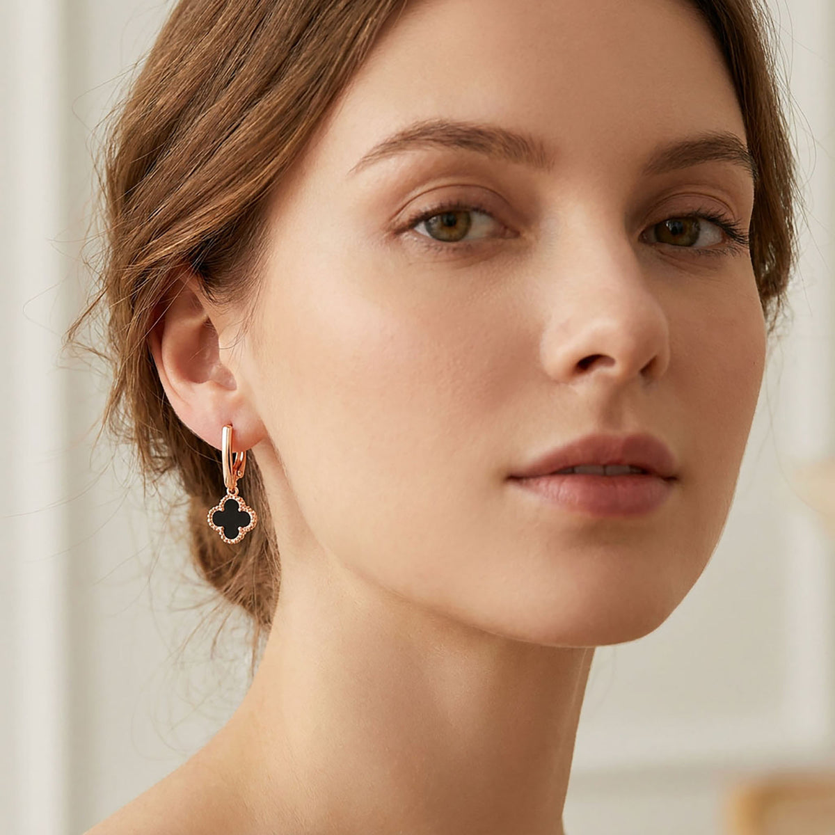 Earring with a black enamel four-leaf clover in a gold-tone frame and leverback clasp on a model's ear