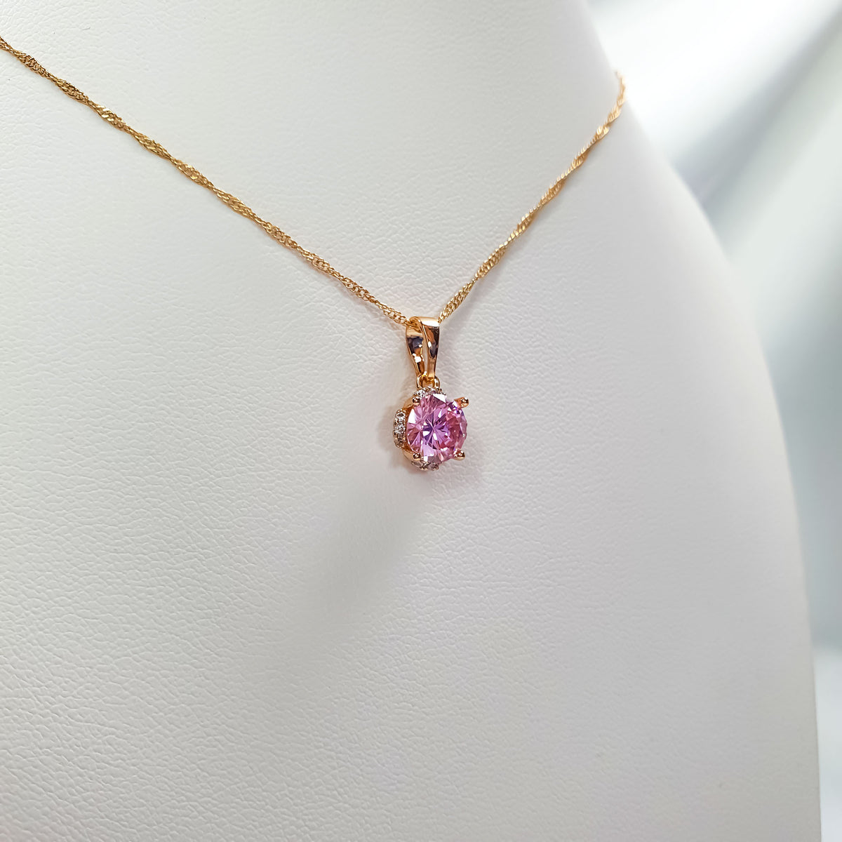 Close-up of pink pendant on a twisted gold-tone chain, light jewellery stand