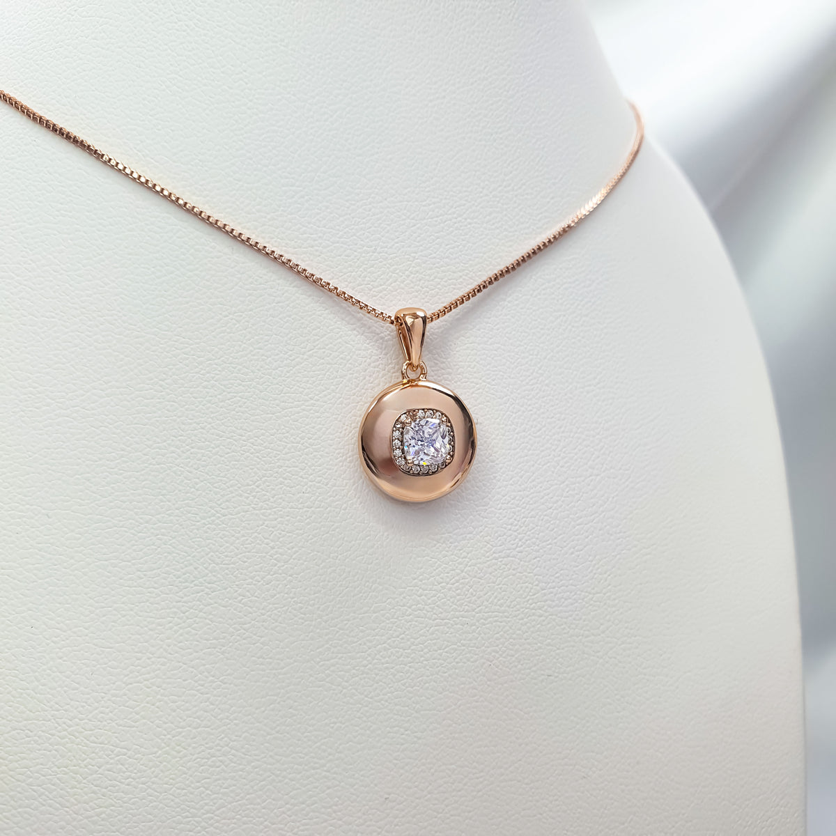 Close-up of gold-tone pendant with sparkling cubic zirconia on a white stand