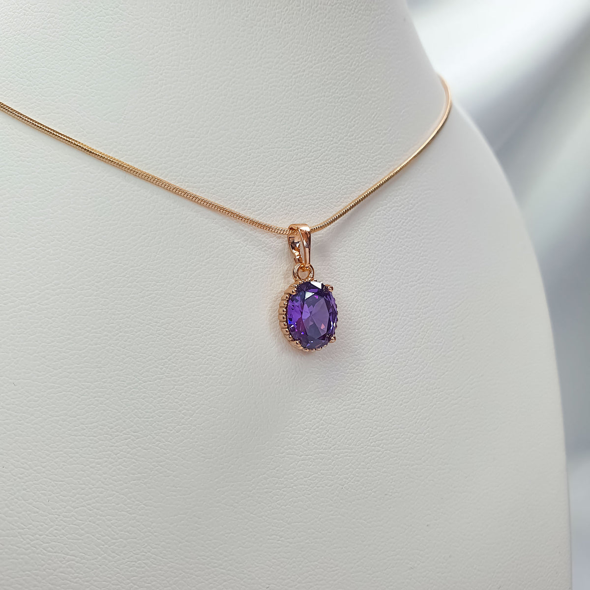 Close-up of violet pendant with lace-like gold-tone edge and thin snake chain