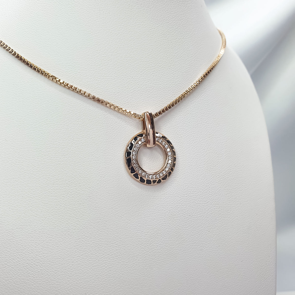 Pendant with black enamel and cubic zirconia circle on a gold-tone chain, white stand