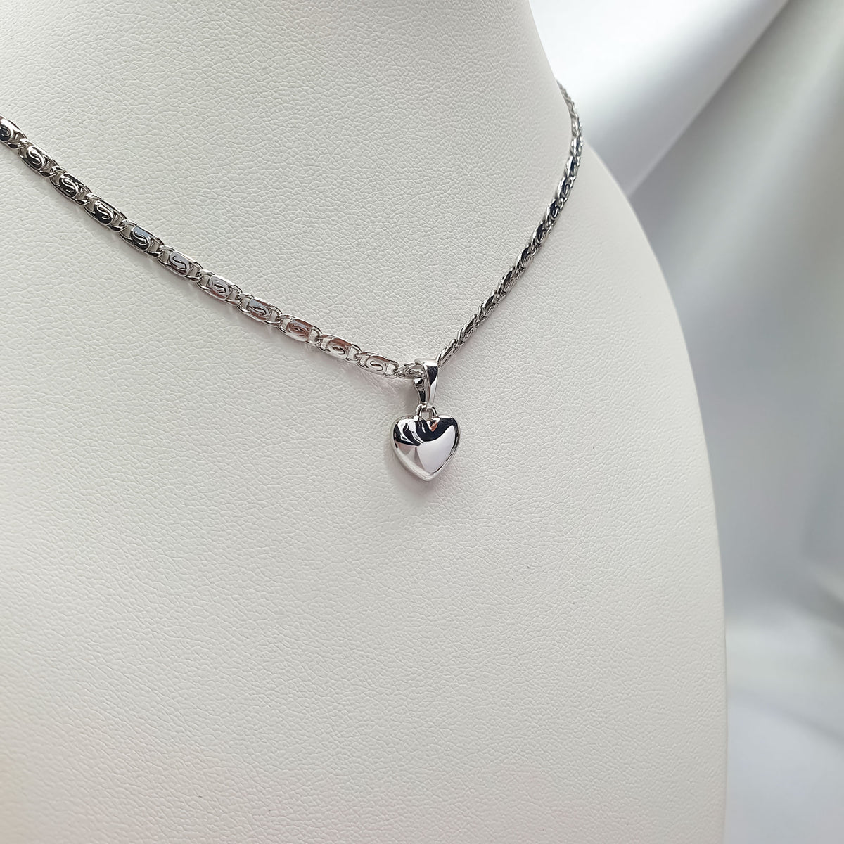 Shiny heart pendant on a silver-tone chain on a white jewellery stand