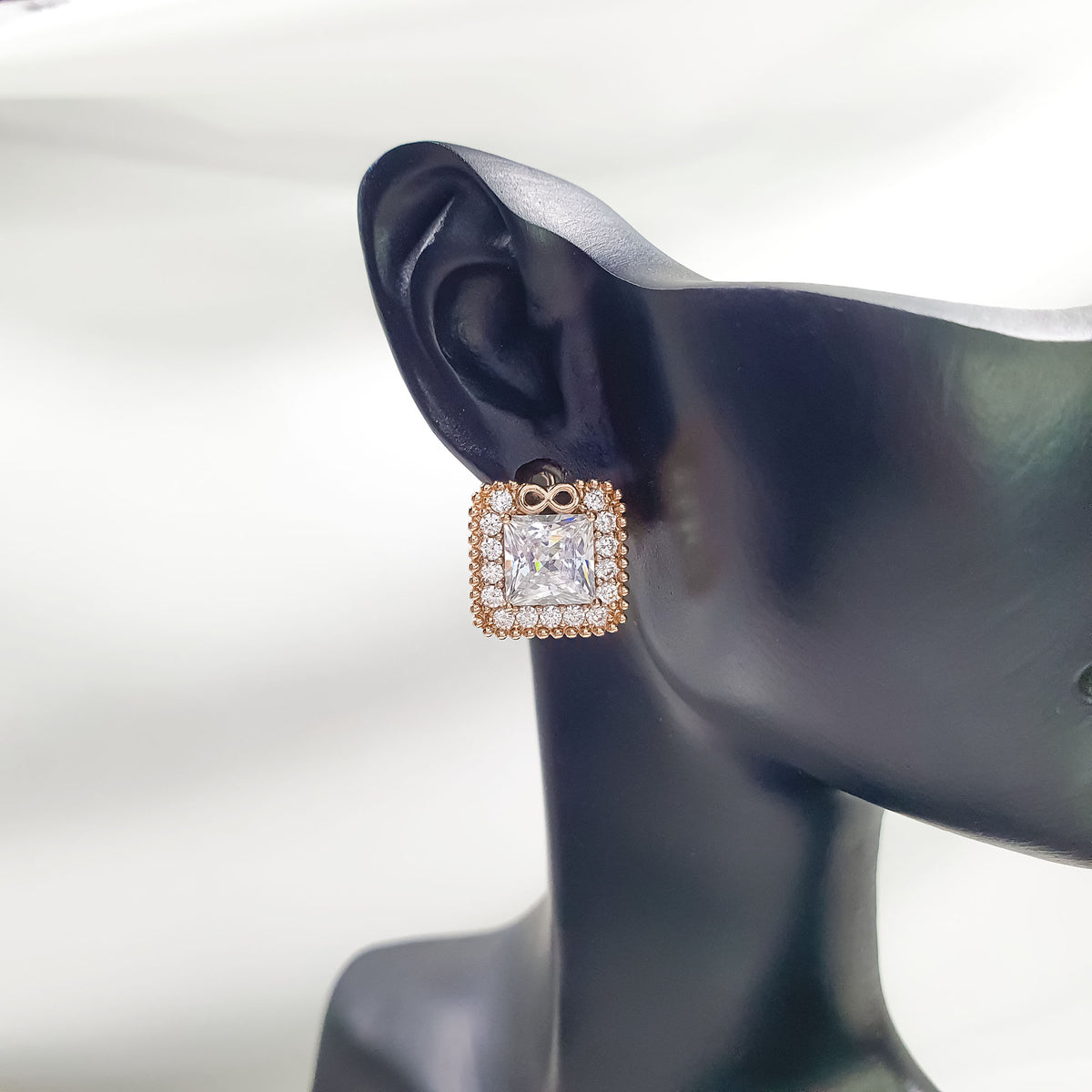 Square earring with gold-tone edge and infinity sign on a dark ear model