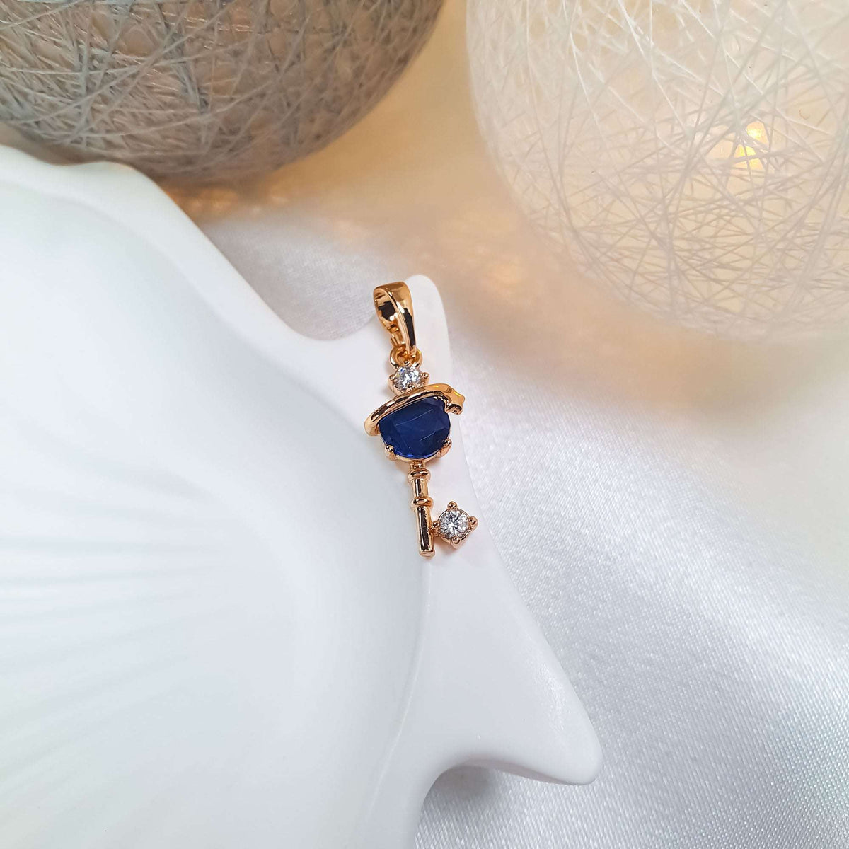Gold-plated key pendant with a blue stone on a ceramic jewellery stand