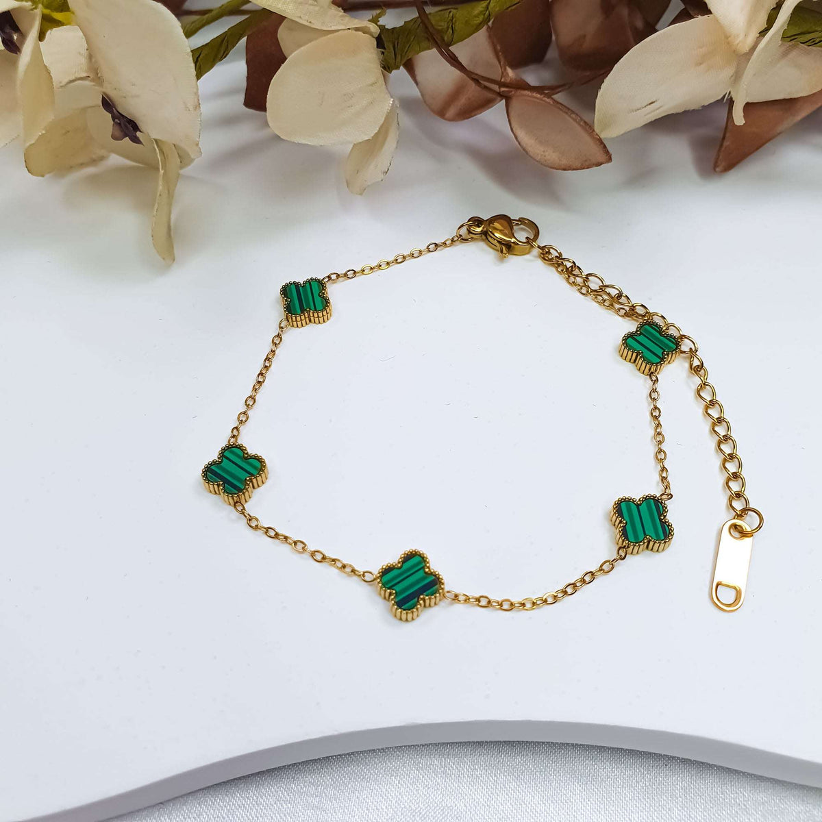 Green clover bracelet laid on a light tray beside beige fabric flowers