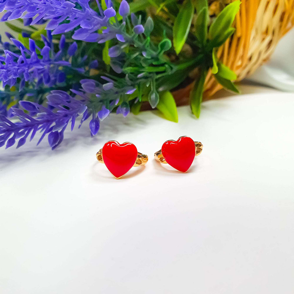 Two gold-plated enamel heart earrings on a white table with lavender behind