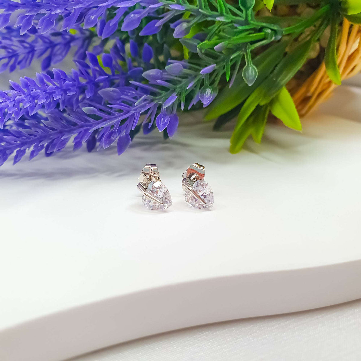 Side view of silver-tone heart cubic zirconia studs beside lavender