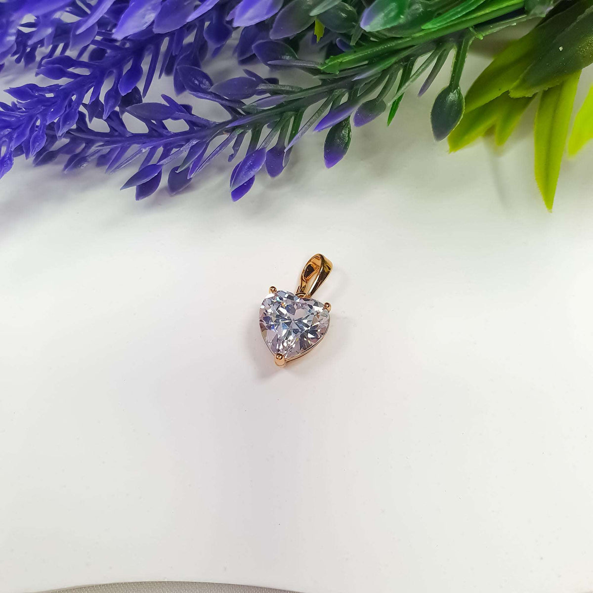 Heart cubic zirconia pendant with a gold-plated bail beside lavender