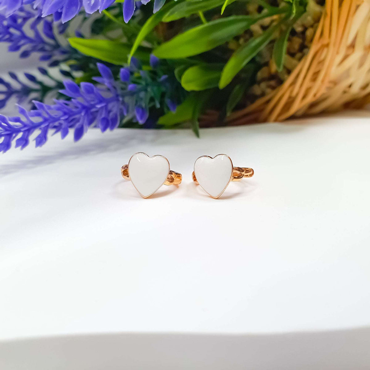 Close-up of white enamel heart earrings in gold tone beside lavender