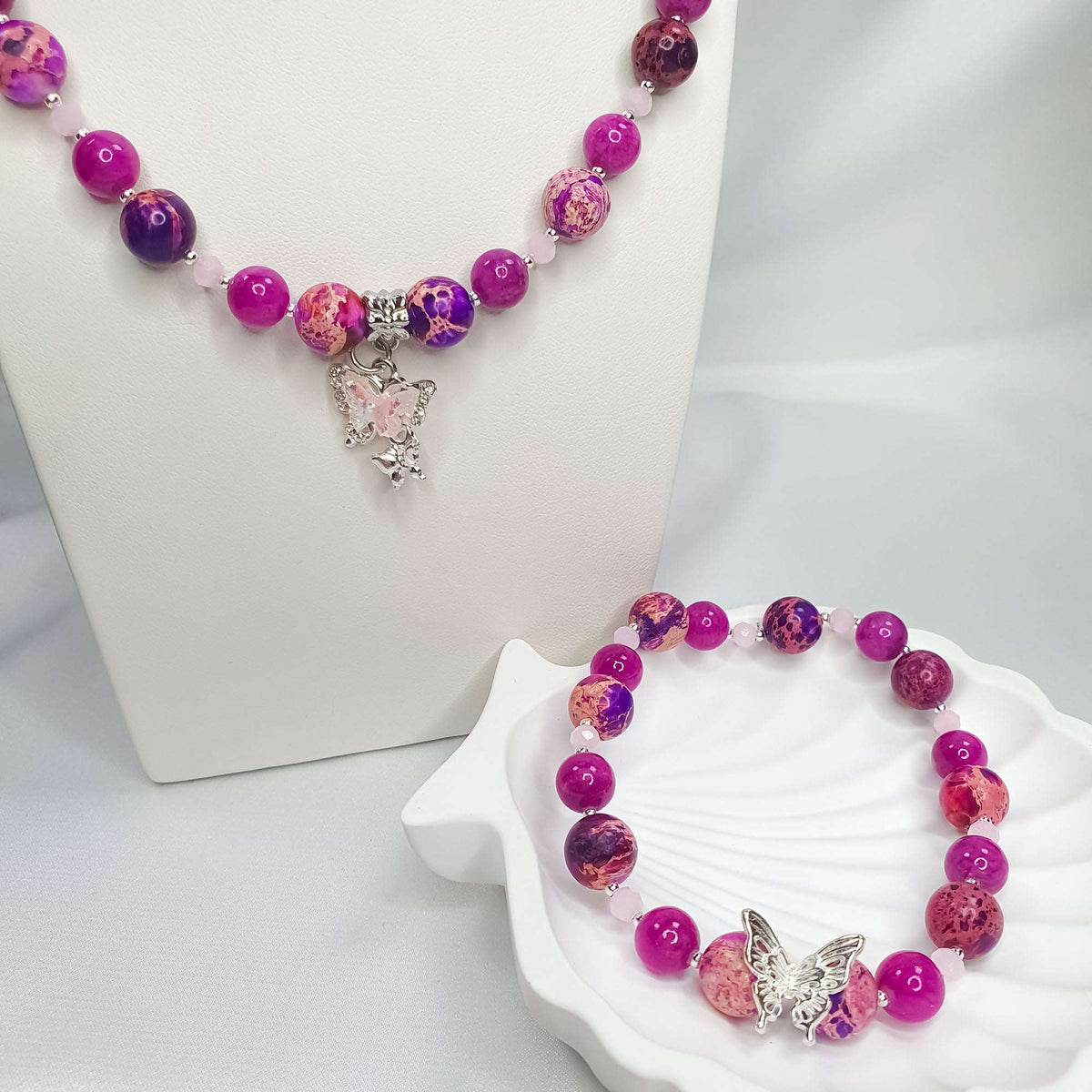 Pink bead necklace with butterfly pendant on a stand, bracelet on a shell
