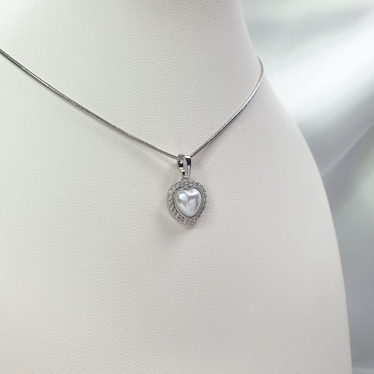 Close-up of pearl heart pendant with cubic zirconia on a light necklace stand