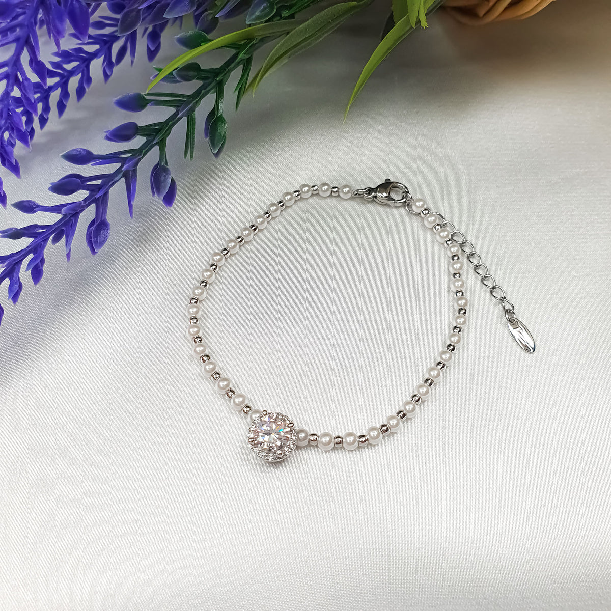 Pearl bracelet with cubic zirconia rosette and lobster clasp on light fabric beside flowers