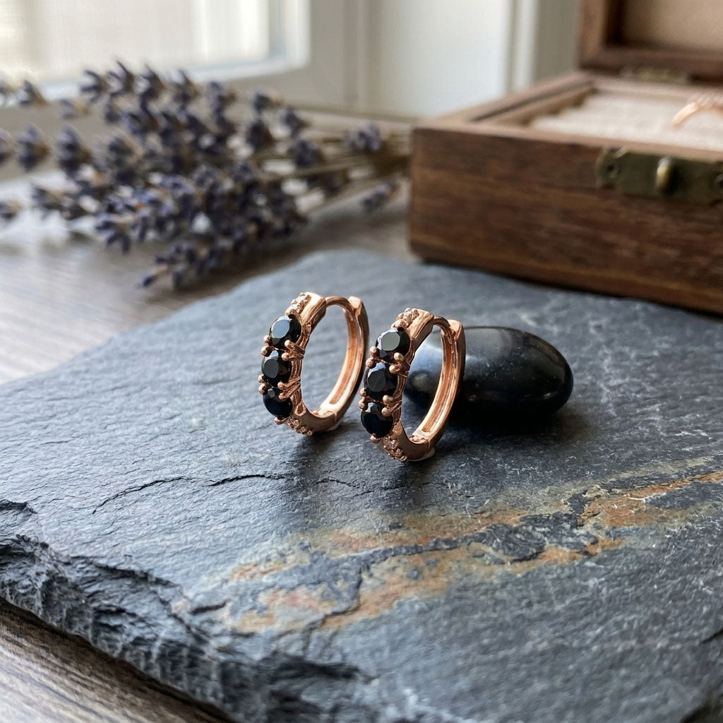 Pair of hinged hoops with black cubic zirconia on dark slate beside dried lavender