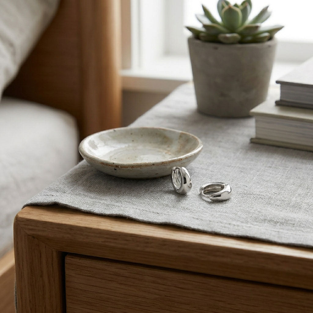 Pair of smooth platinum-plated hoops on light linen beside a ceramic dish