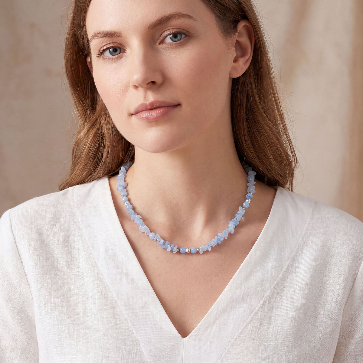 Woman in a white linen blouse wearing a light blue stone necklace