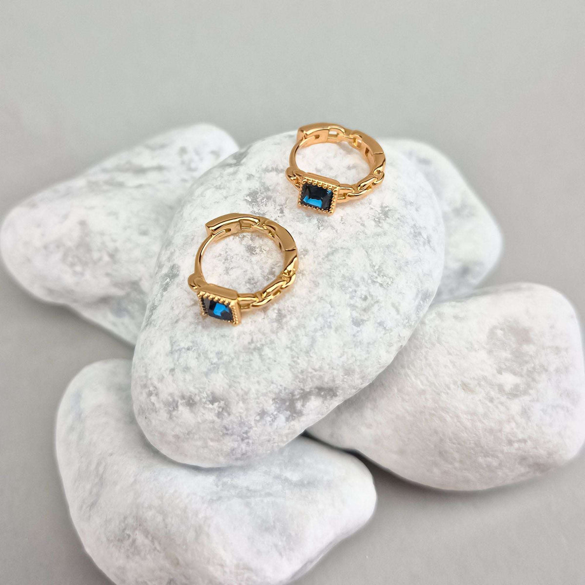 Gold-tone hoop earrings with a blue stone on white pebbles, chain texture in profile
