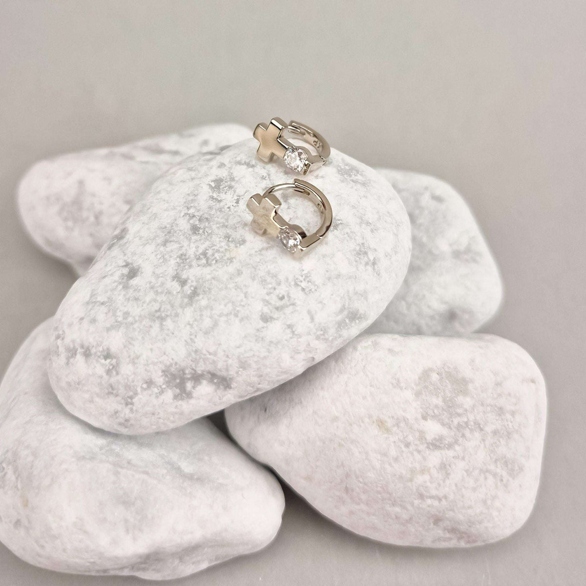 Silver-tone cross earrings with leverback clasps, side view on white pebbles