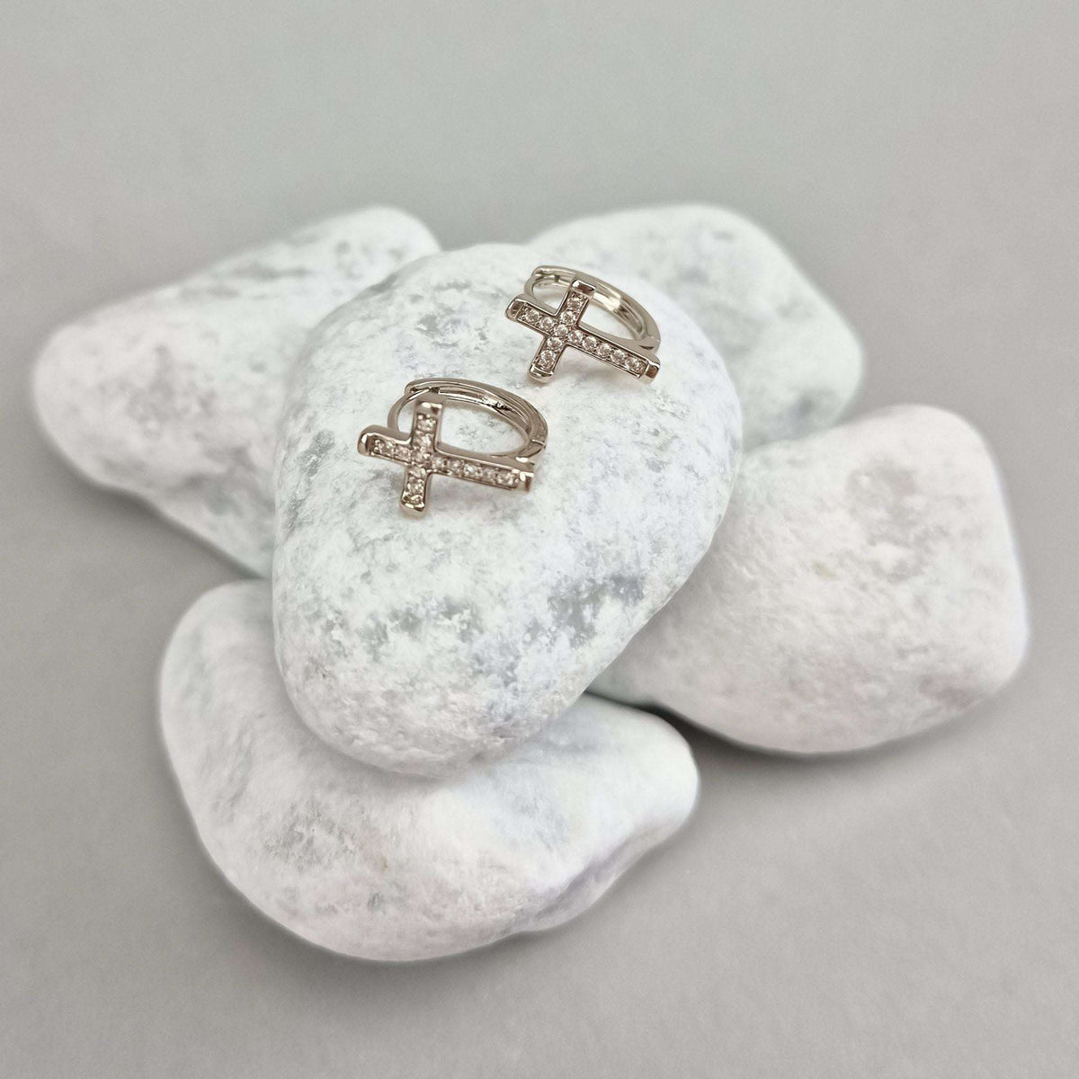 Close-up of silver-tone cross earrings with leverback clasps on white stones