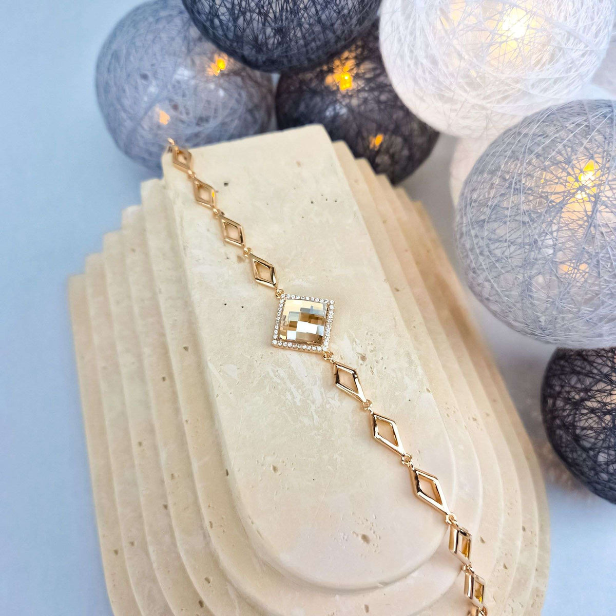 Gold-plated rhombus link bracelet with a sparkling crystal on a stone stand, warm lights