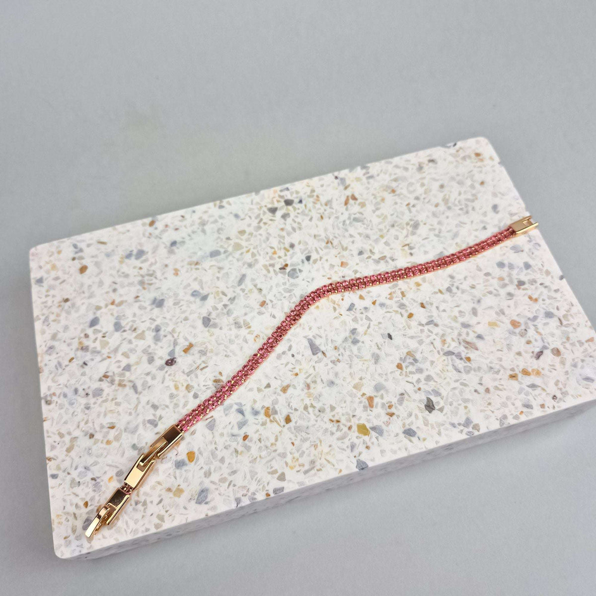 Slim pink crystal bracelet with an open gold-plated clasp on a terrazzo slab