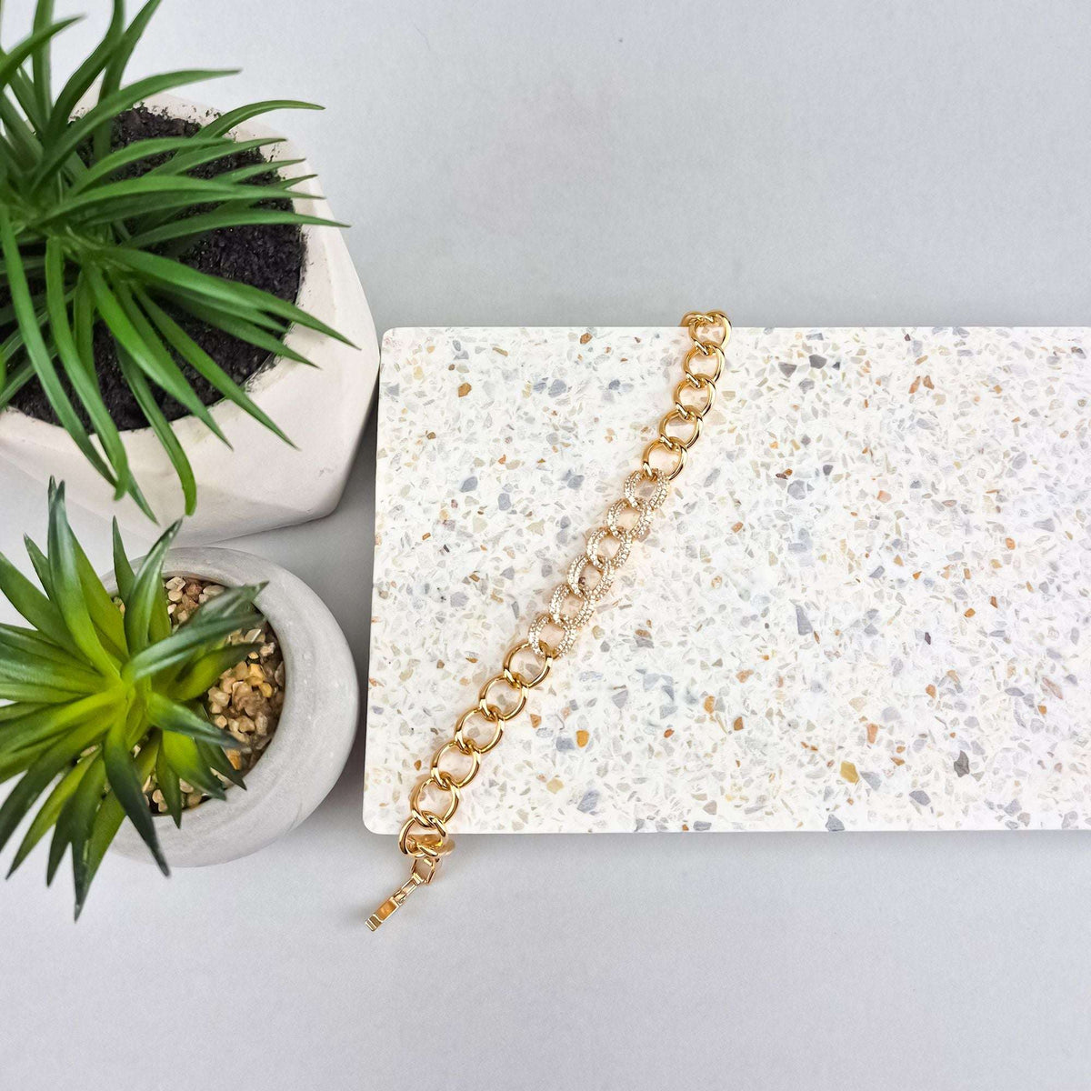 Gold-tone link bracelet on a terrazzo slab next to green succulents