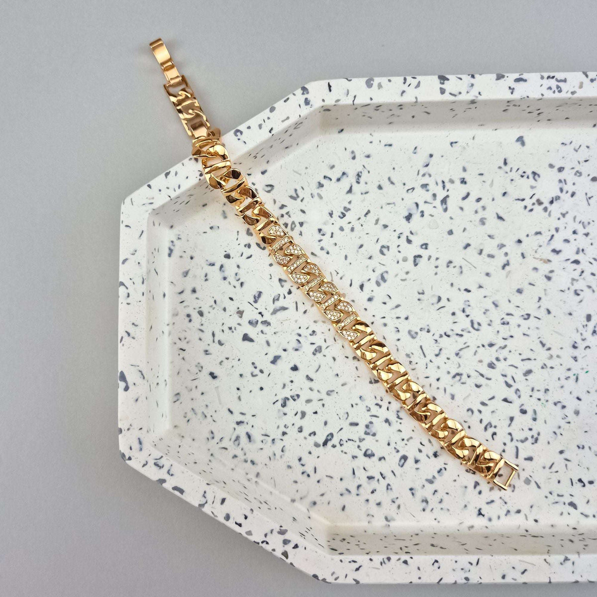Gold-tone bracelet with sparkling cubic zirconia laid out on a white speckled ceramic tray