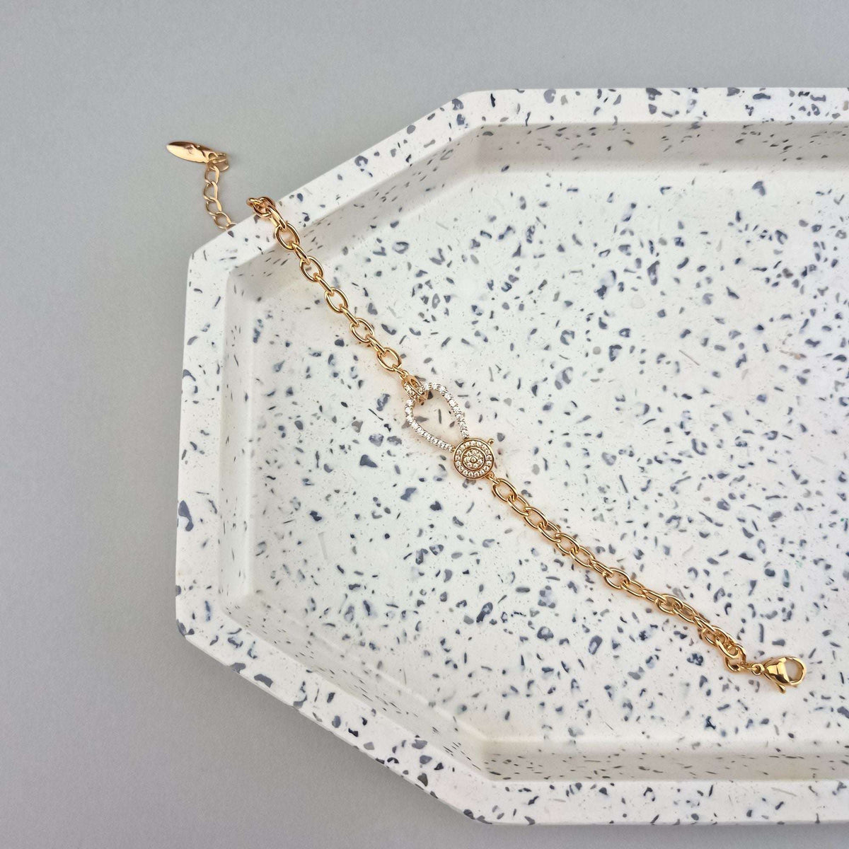Gold-plated chain bracelet with a zirconia-set oval link on a light decorative tray