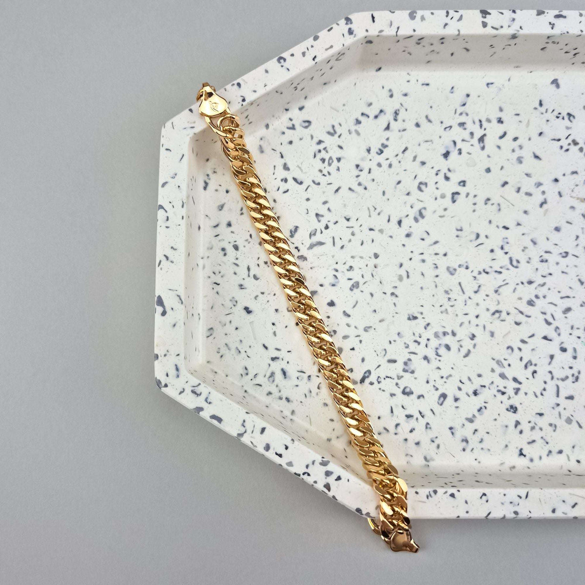 Gold-plated Cuban-style link bracelet on a speckled ceramic tray, close-up