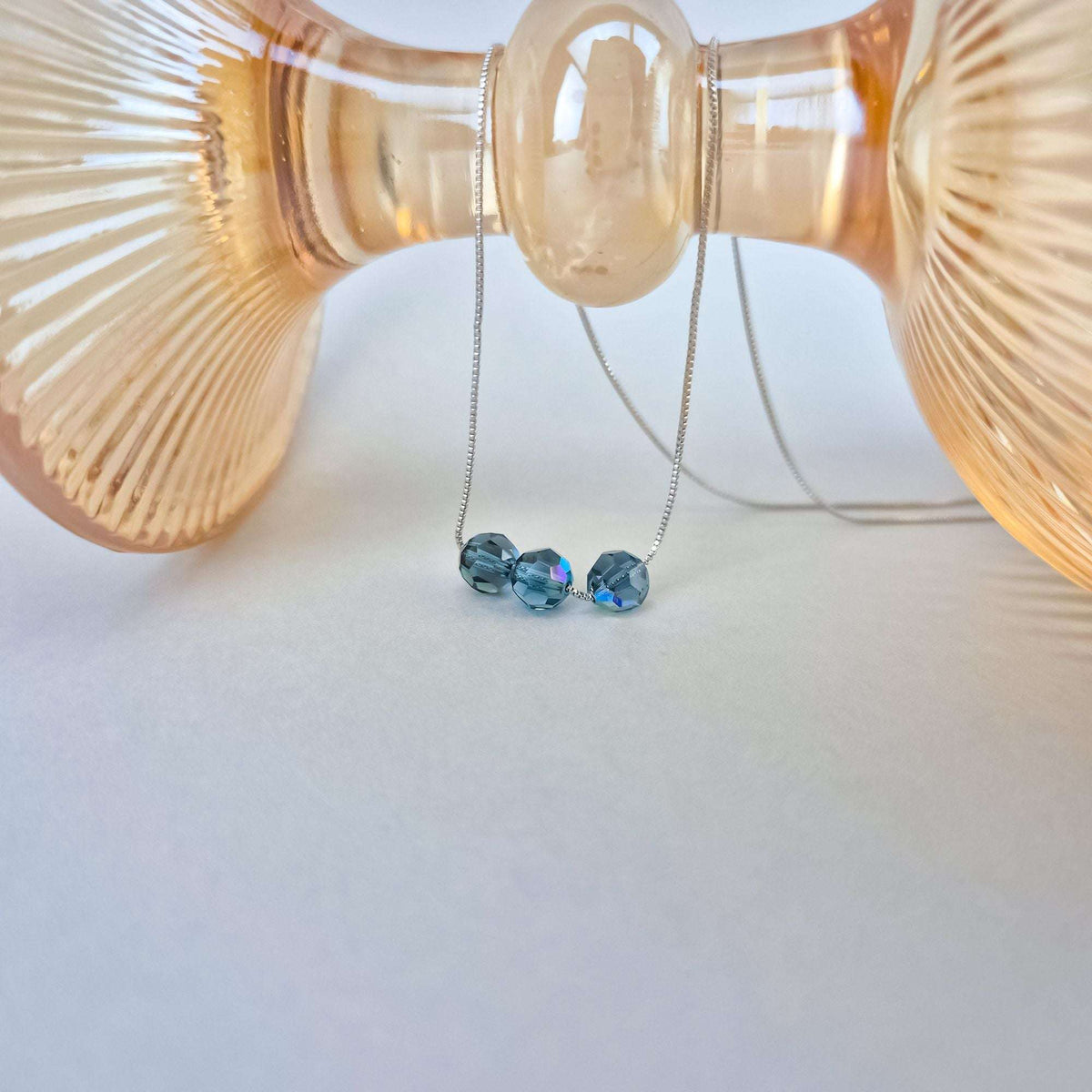 Silver-tone crystal necklace draped over a pale peach glass dish