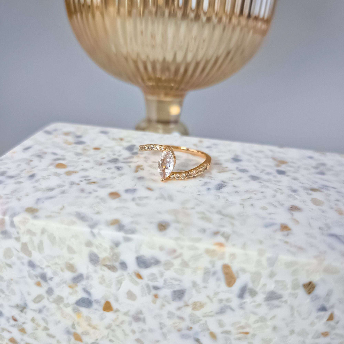 Gold-plated ring with an elongated faceted crystal and side stones on light stone