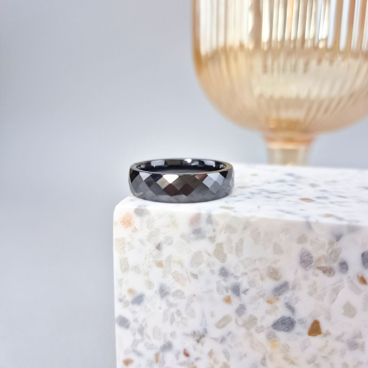 Faceted black ceramic ring standing on light terrazzo, gold lamp behind
