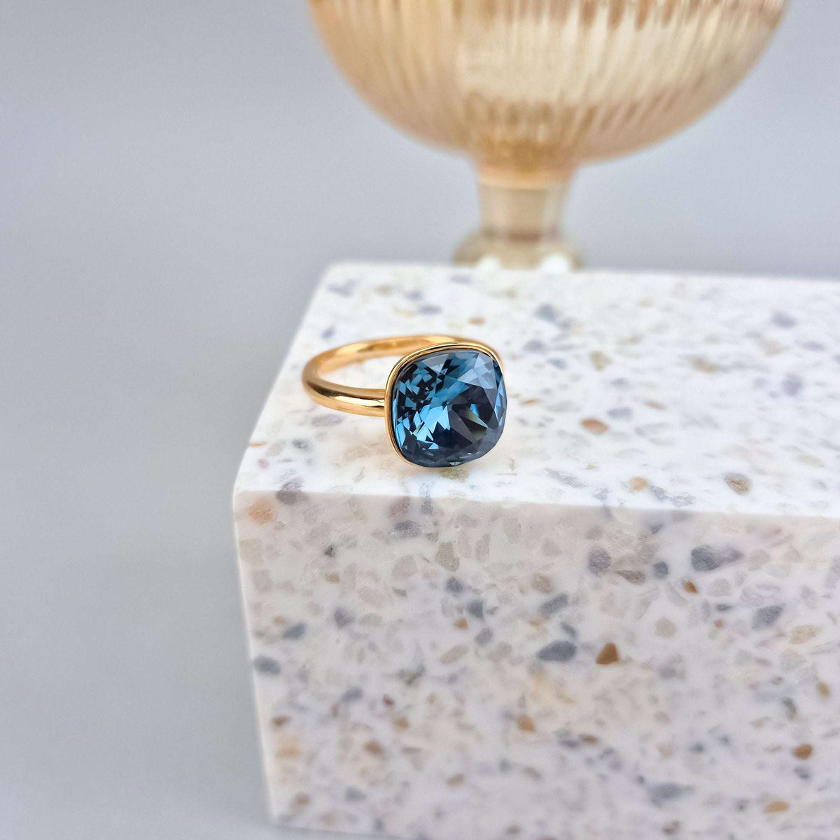 Gold-plated ring with a large square blue crystal on light terrazzo