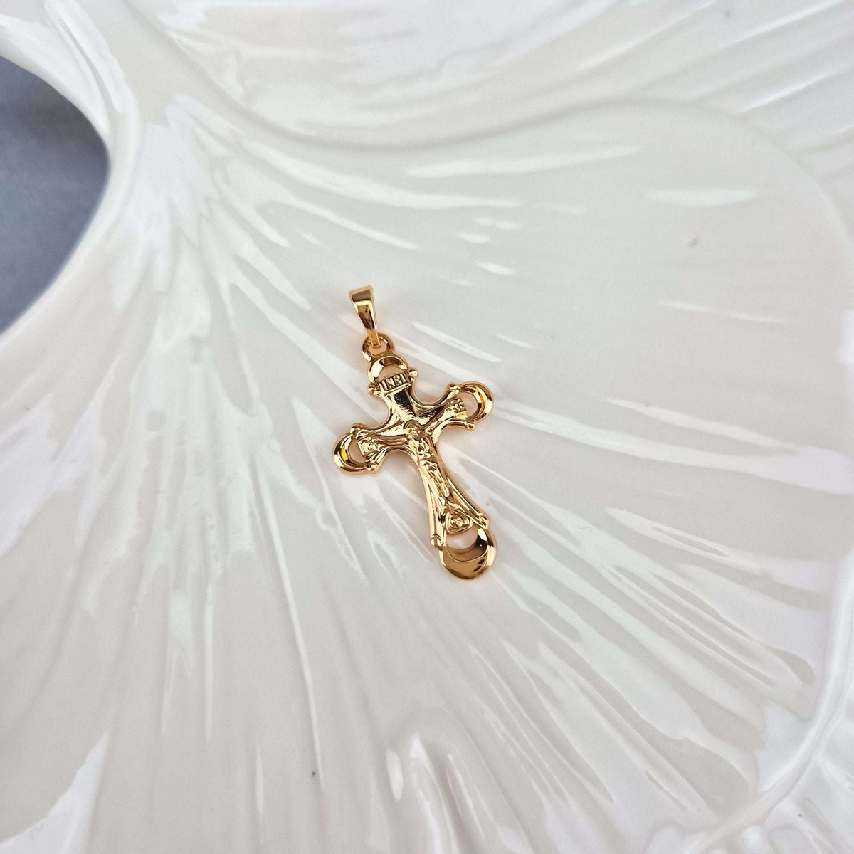 Catholic cross pendant at an angle on a white ceramic leaf, warm gold shine