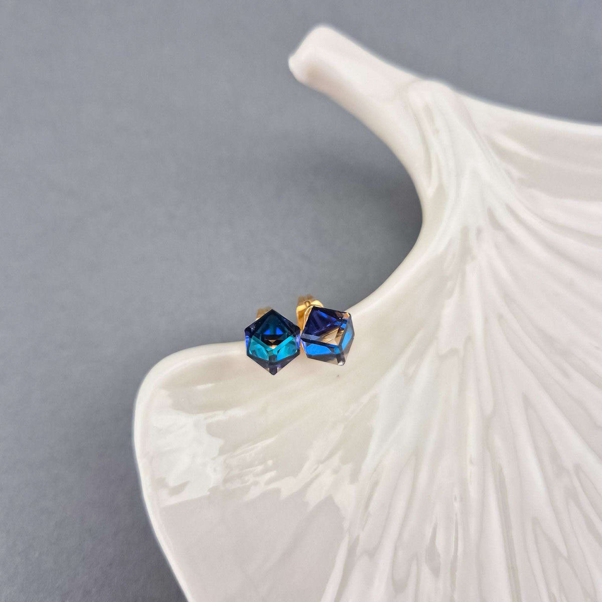 Crystal cube studs on a white ceramic leaf, gold-tone post and turquoise glints