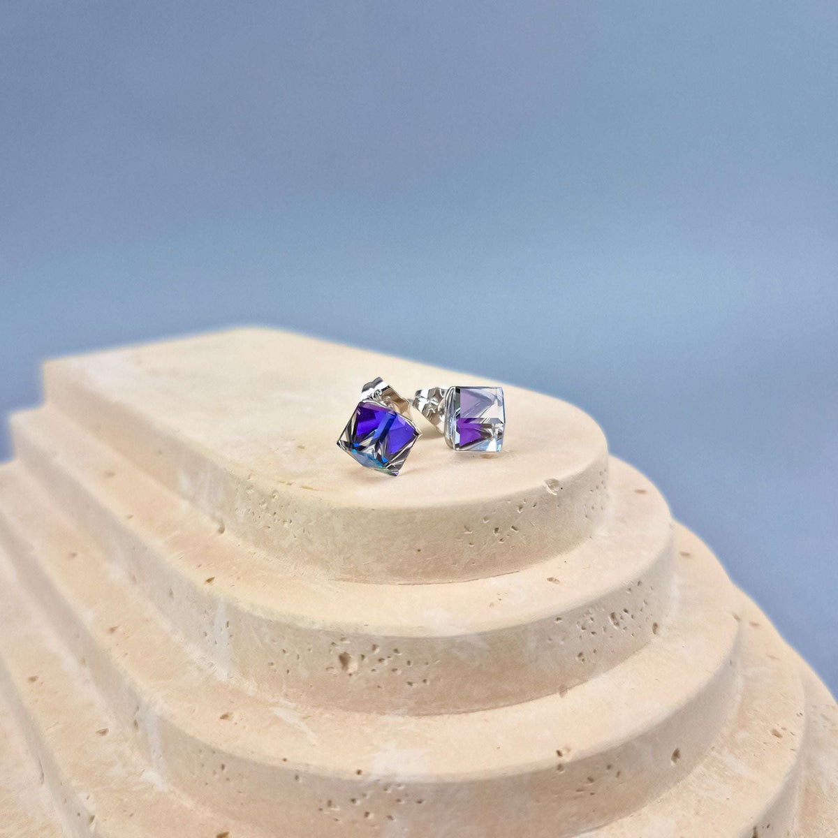 Pair of cube crystal studs with platinum-tone posts on a light stone stand